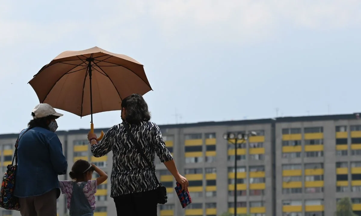 Tres personas utilizan una sombrilla para cubrirse de los rayos del sol.