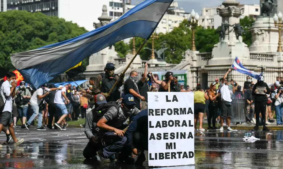 MALESTAR. Manifestantes se cubren con una manta del chorro de agua lanzado por la policía durante la protesta contra la reforma laboral, en Buenos Aires.