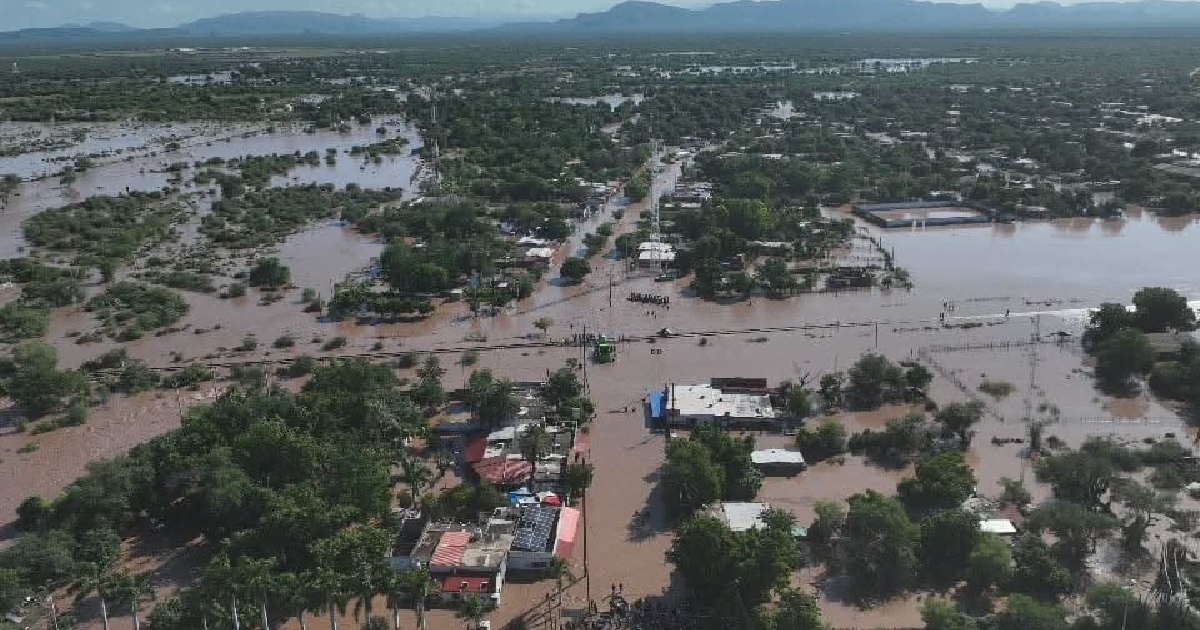 Vista aérea con dron en plano general que muestra severas inundaciones en un poblado y zonas rurales de Sonora. El agua café y turbia anegó calles, caminos, campos agrícolas y viviendas, cubriendo amplias extensiones de terreno entre los árboles y las estructuras habitacionales.